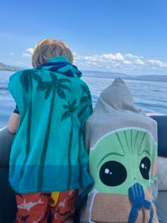 two young kids look over the side of a boat on a lake