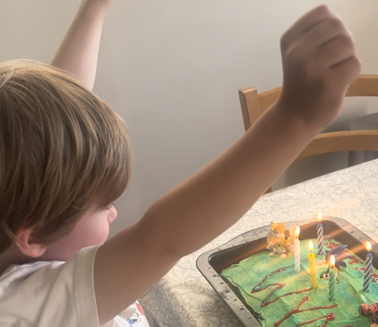a young blonde boy in front of a green birthday cake with lit candles