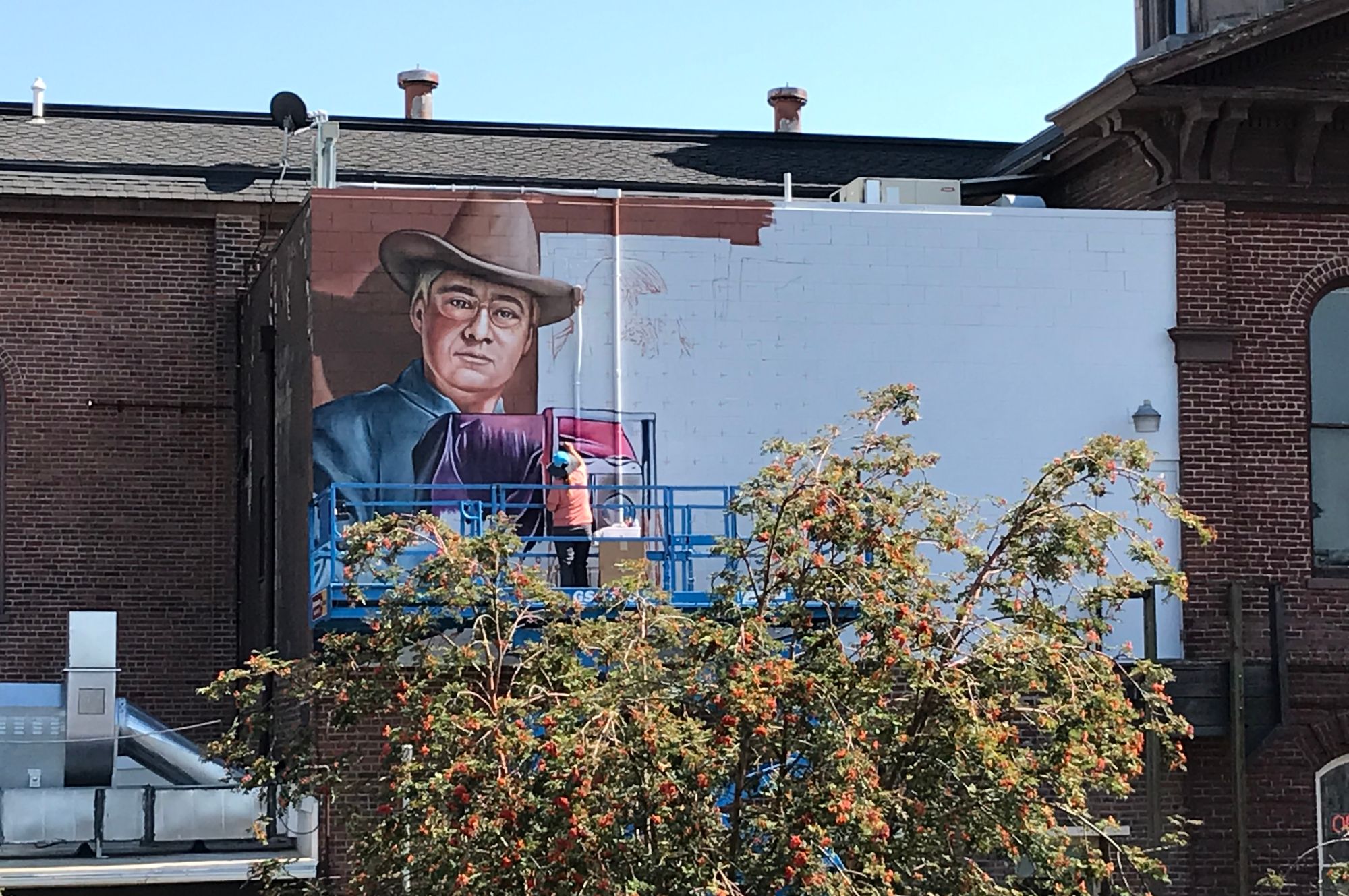 Person on a platform painting a mural high up on a wall.