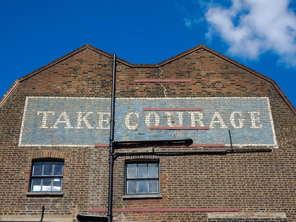 View of upper portion of a brick building with a hand-painted sign that reads "Take Courage".