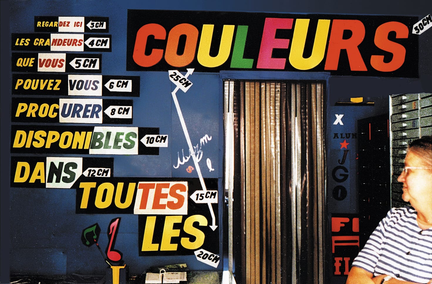 Woman looking at a wall adorned with colourful letters mounted to form a wall display showing their availability in different sizes.