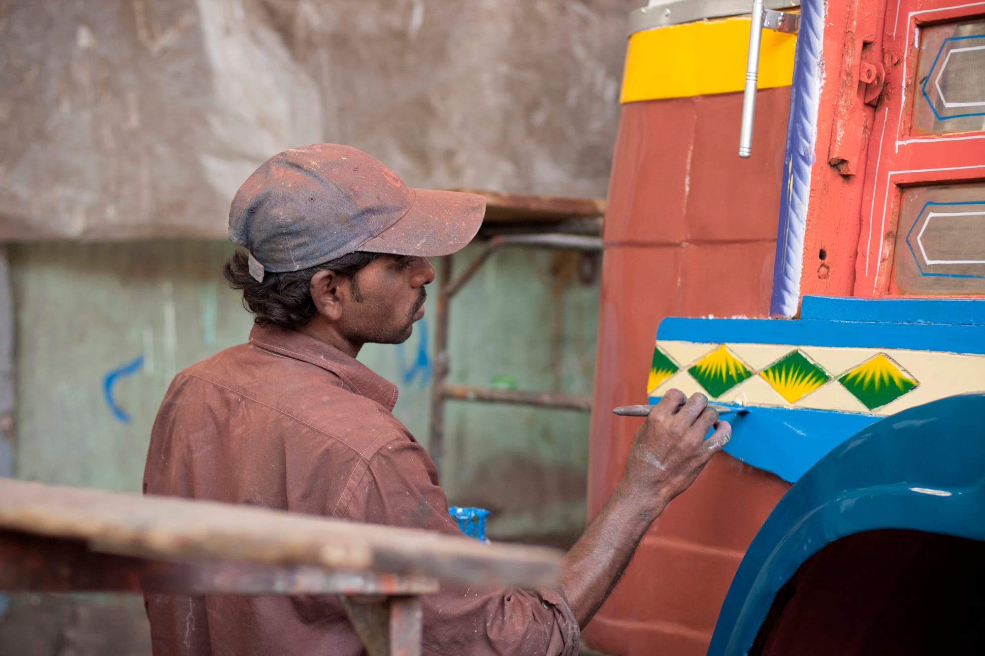 Man in a baseball cap applying blue paint to decorations on the side of a vehicle.