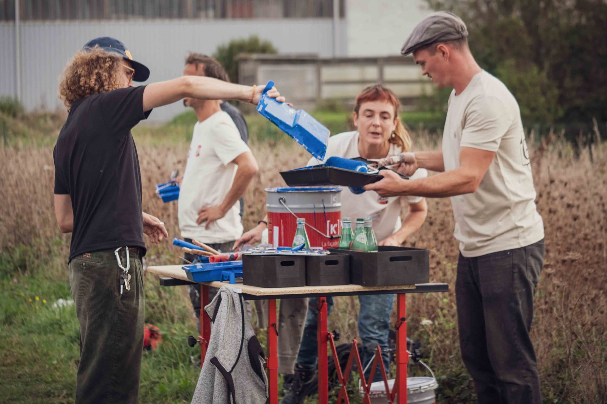 People gathered around a table, with one pouring paint from one rolling tray into another.