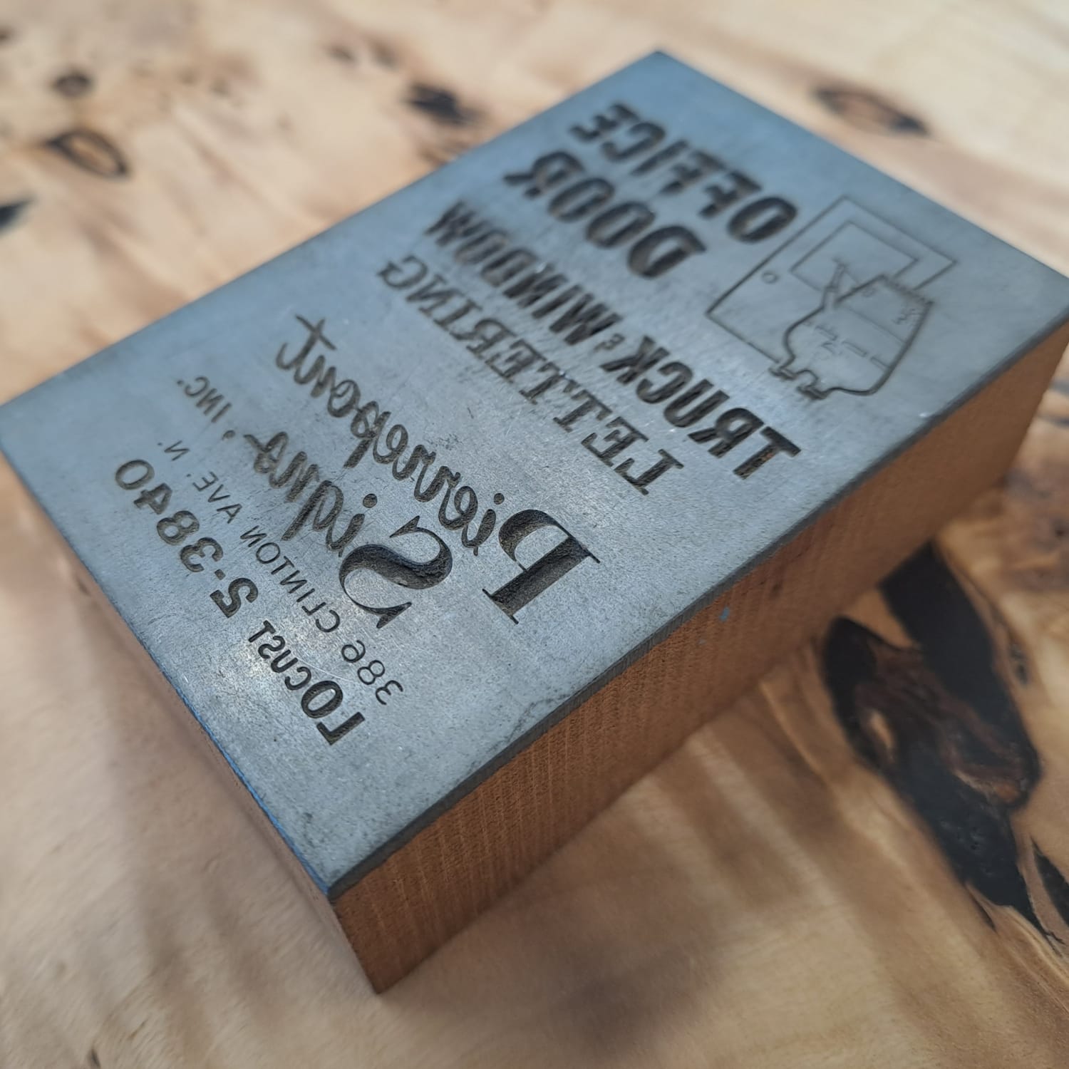 Printing block with an advertisement for Pierrepont signs engraved into the metal face that's mounted onto a piece of wood.