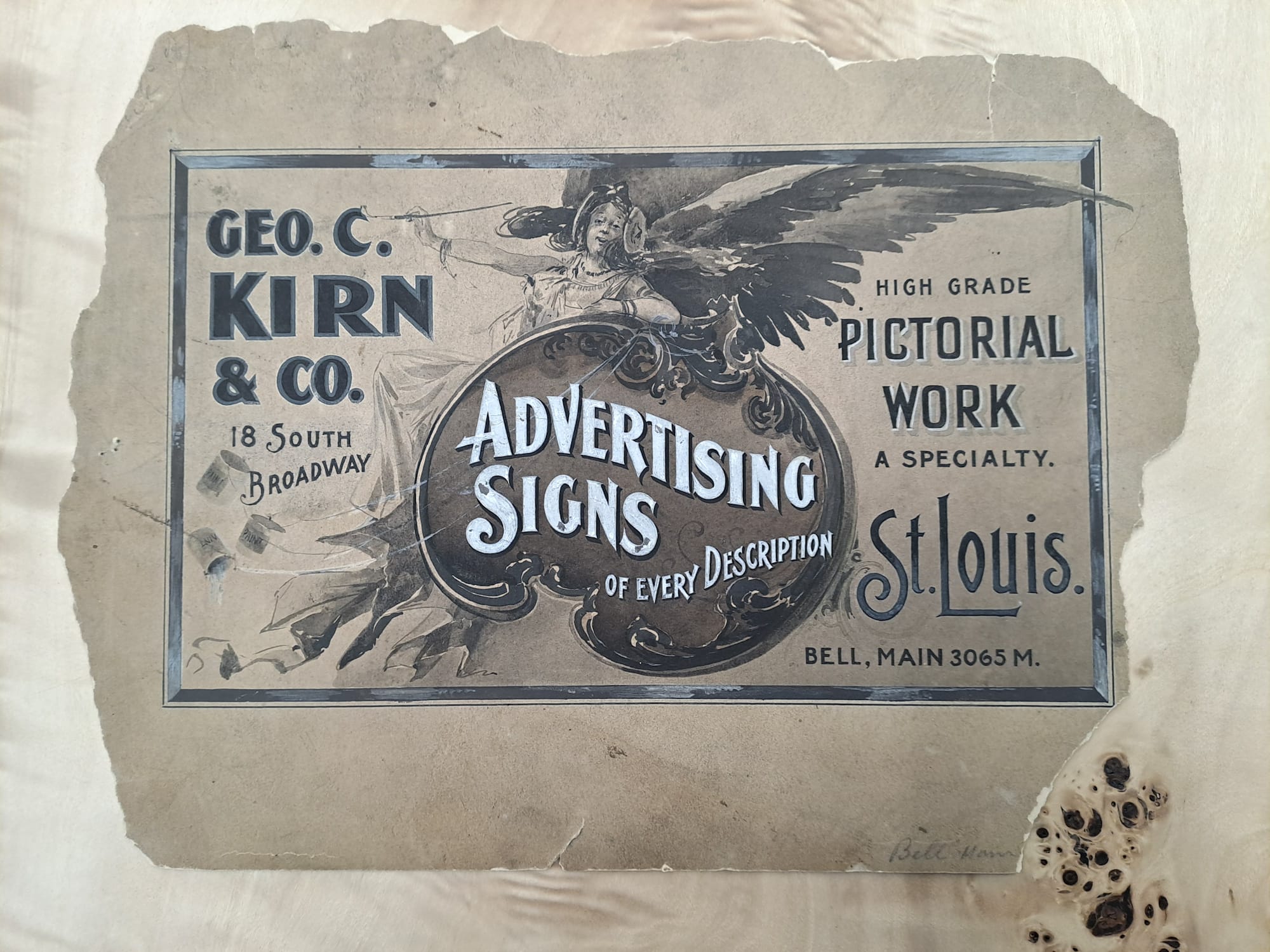 Hand-drawn and painted advertisement on old paper that advertises Geo. C. Kirn & Co. "Advertising Signs of Every Description, High Grade Pictorial Work a Specialty". The first part of this copy is set within a decorative panel, behind which there is a winged woman reclining as she paints the C in Geo C. Kirn's name.