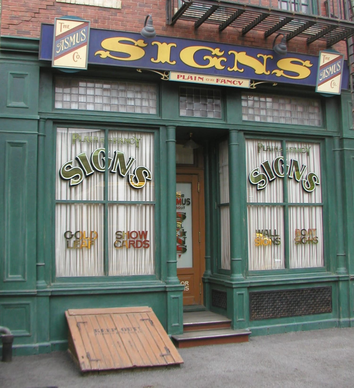 Shopfront for a sign firm. In addition to a large fascia sign that reads 'SIGNS, Plain or Fancy, The Asmus Co.', there are gilded and painted signs in the window.