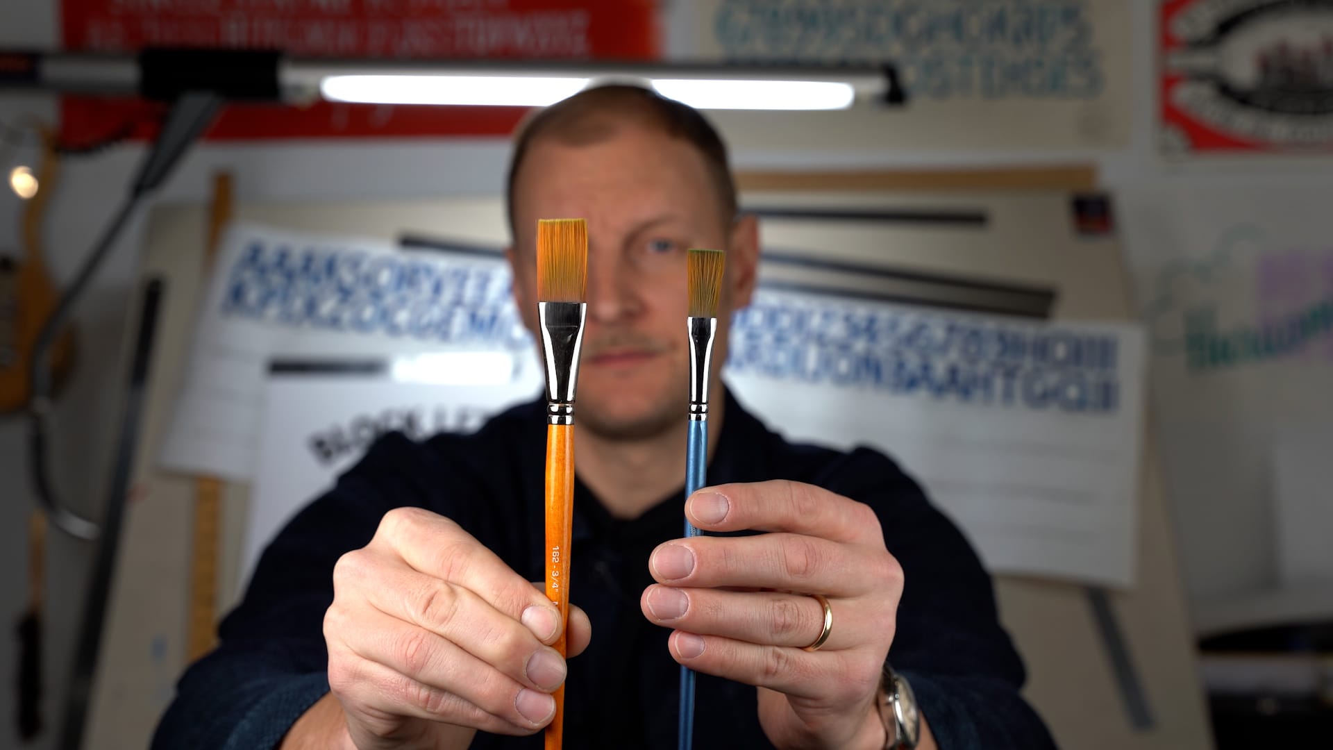 Man holding two flat brushes, one larger than the other, in front of his face.