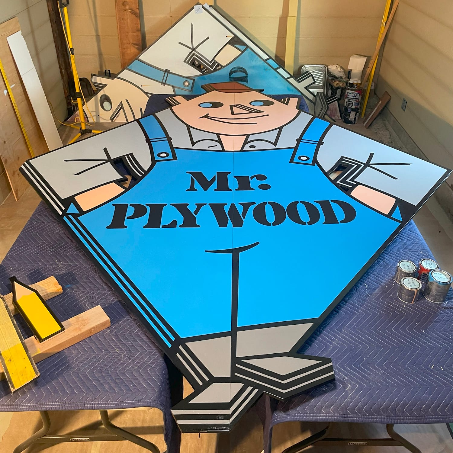The finished replica of the Mr. Plywood sign laid flat on e workbenches in a shed setting.