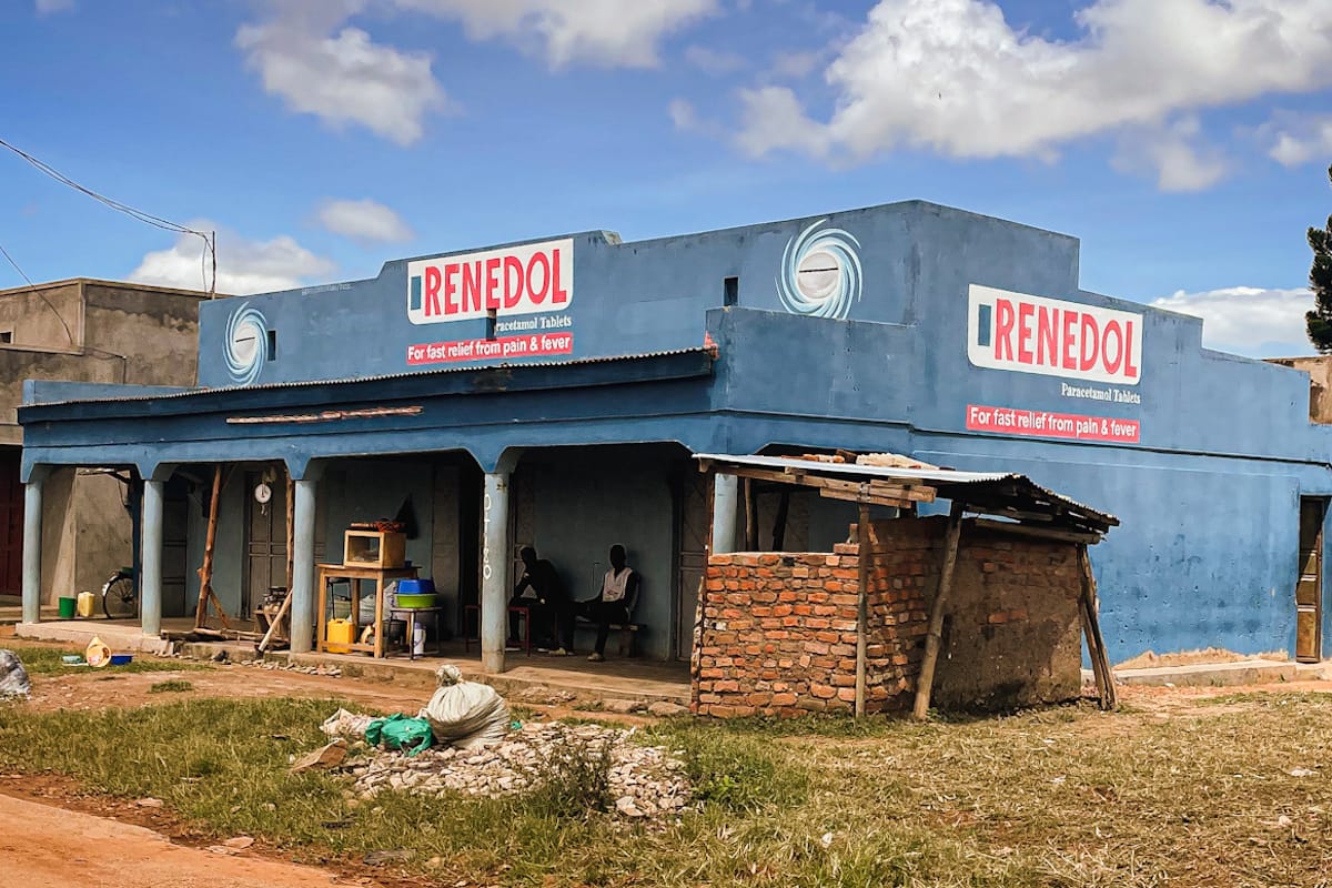 Large lowrise building all painted in blue with signs on the front and side advertising the Renedol brand, which is lettered in red on a white background. Just beyond the building is another that has no exterior decoration and is just bare grey concrete.
