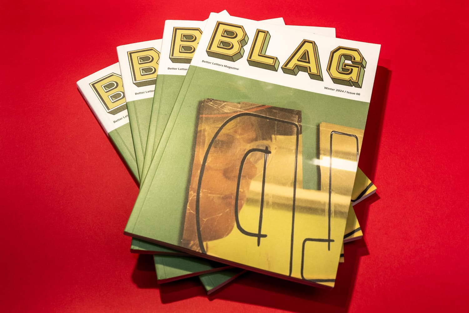 Four identical magazines fanned out. The cover shows a face reflected in sheets of gold leaf on glass while the masthead reads "BLAG".