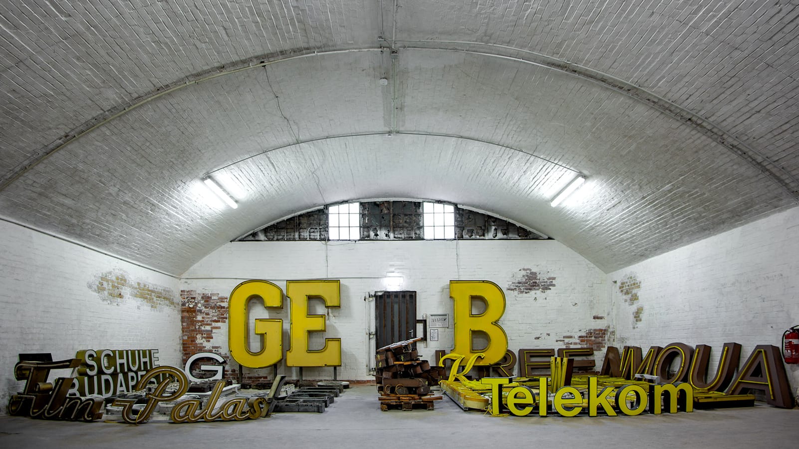 Arrangements of dimensional letters and signs in white and yellow tones in an arched warehouse setting with white walls.
