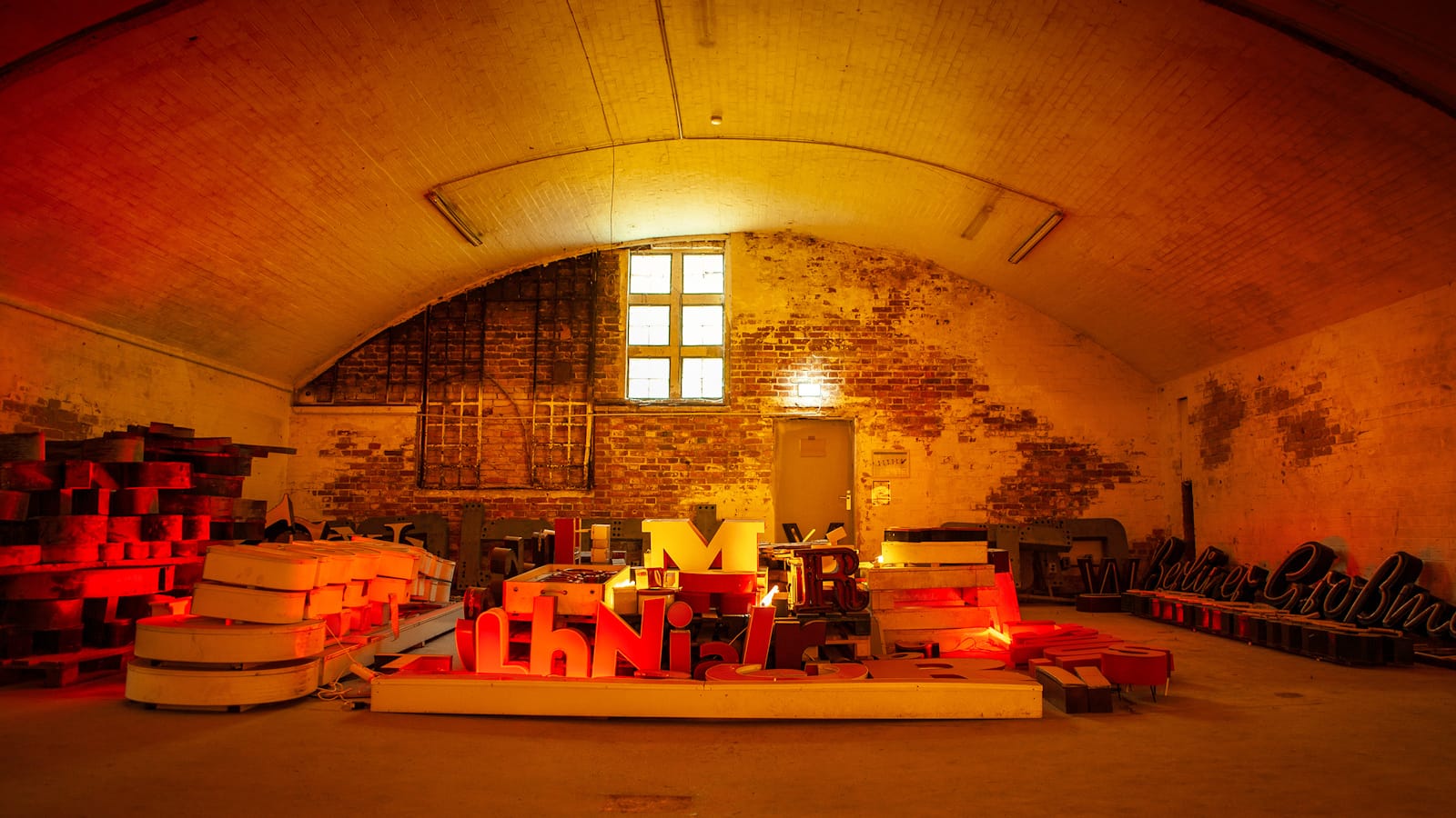 Piles of letters bathed in red-yellow light in an arched warehouse setting.