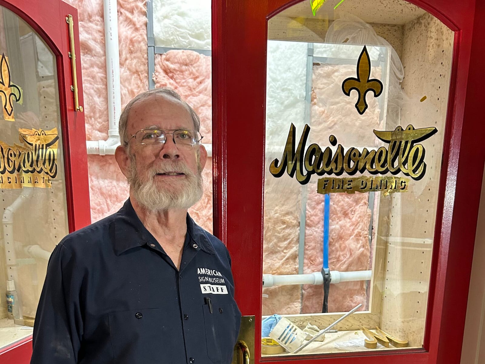 Man standing in front of a double door on which each glass panel has gilded lettering for "Maisonette, Fine Dining".