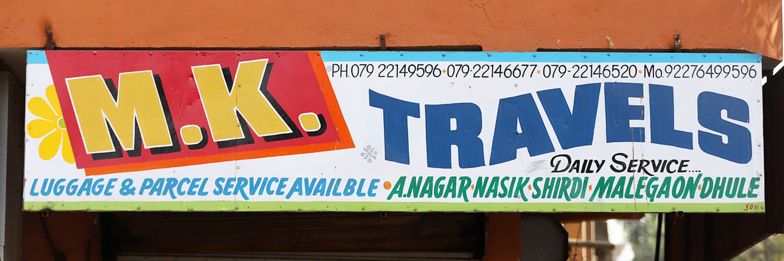 Latin sign for M.K. Travels. The initials are on a red background, and the word “Travels” in blue on a curved baseline.