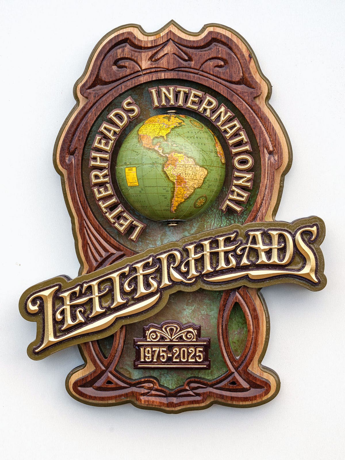 Carved and gilded ornamental wooden sign with a vintage globe set in it. Lettering around the globe reads "Letterheads International" while the main lettering running throught the middle of the panel and protroding from either side says "Letterheads" with a smaller piece below that with the dates "1975–2025".
