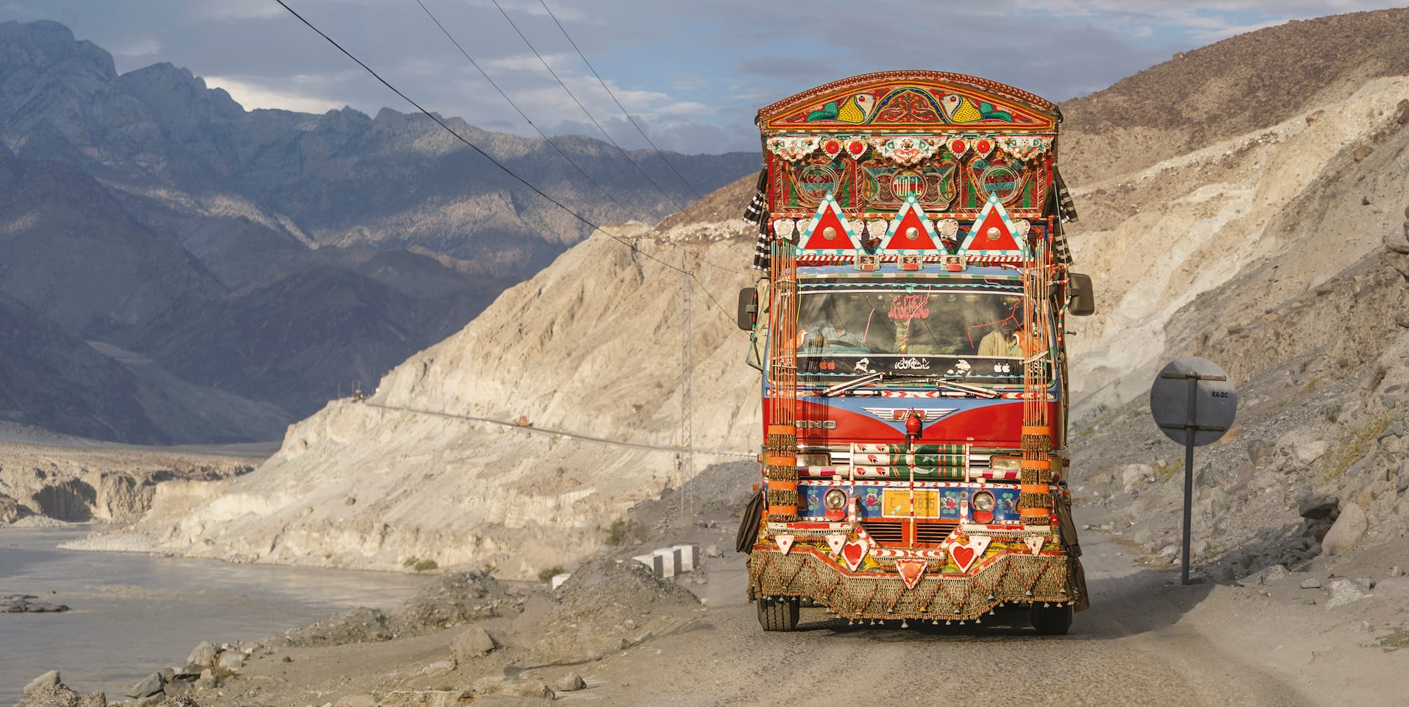Mountain scenery of greys and browns with a brightly coloured and decorated truck framed like a portrait and driving towards the viewer.