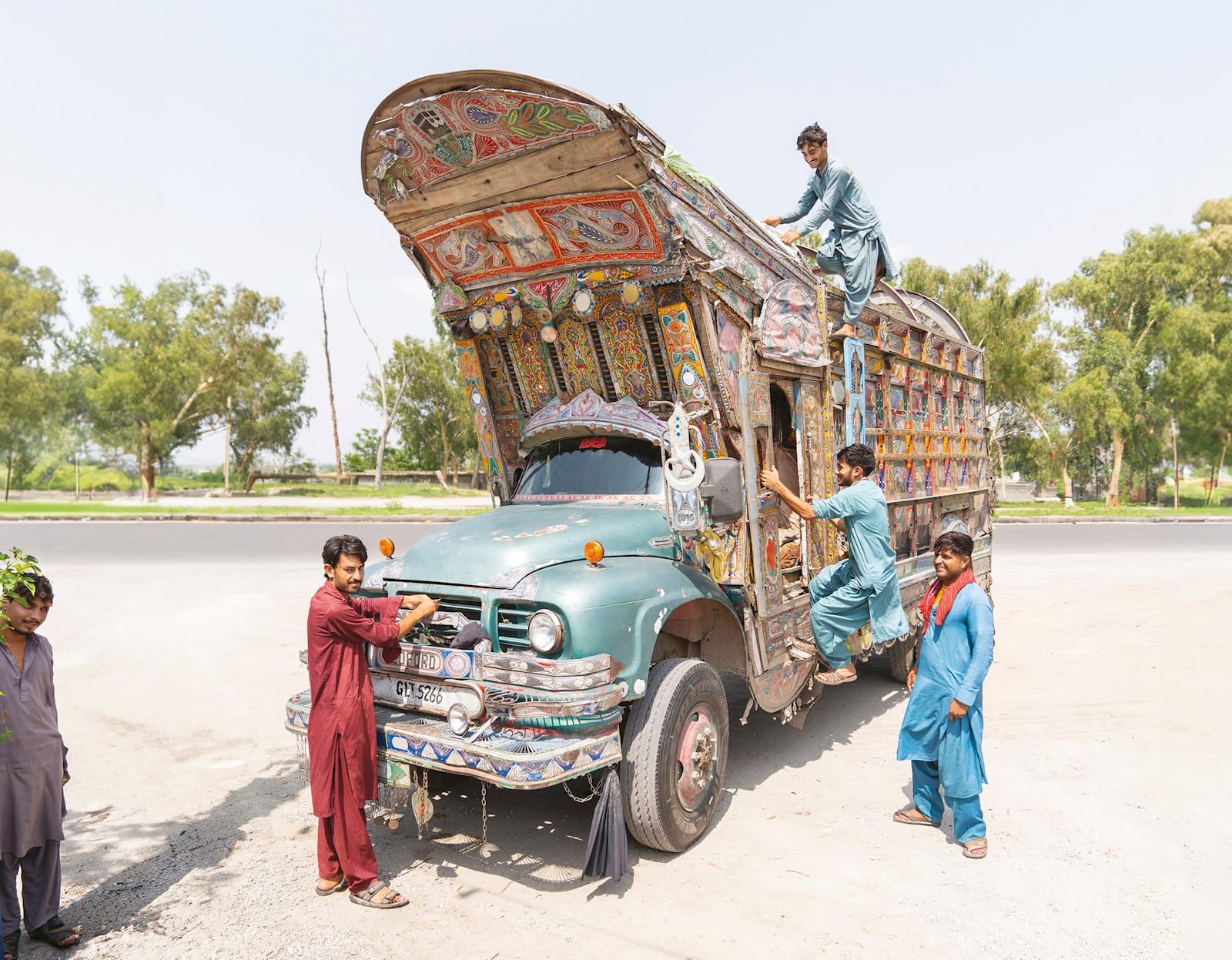 A vintage truck, brightly decorated, with men variously attending to matters on the truck and posing for the photographer.