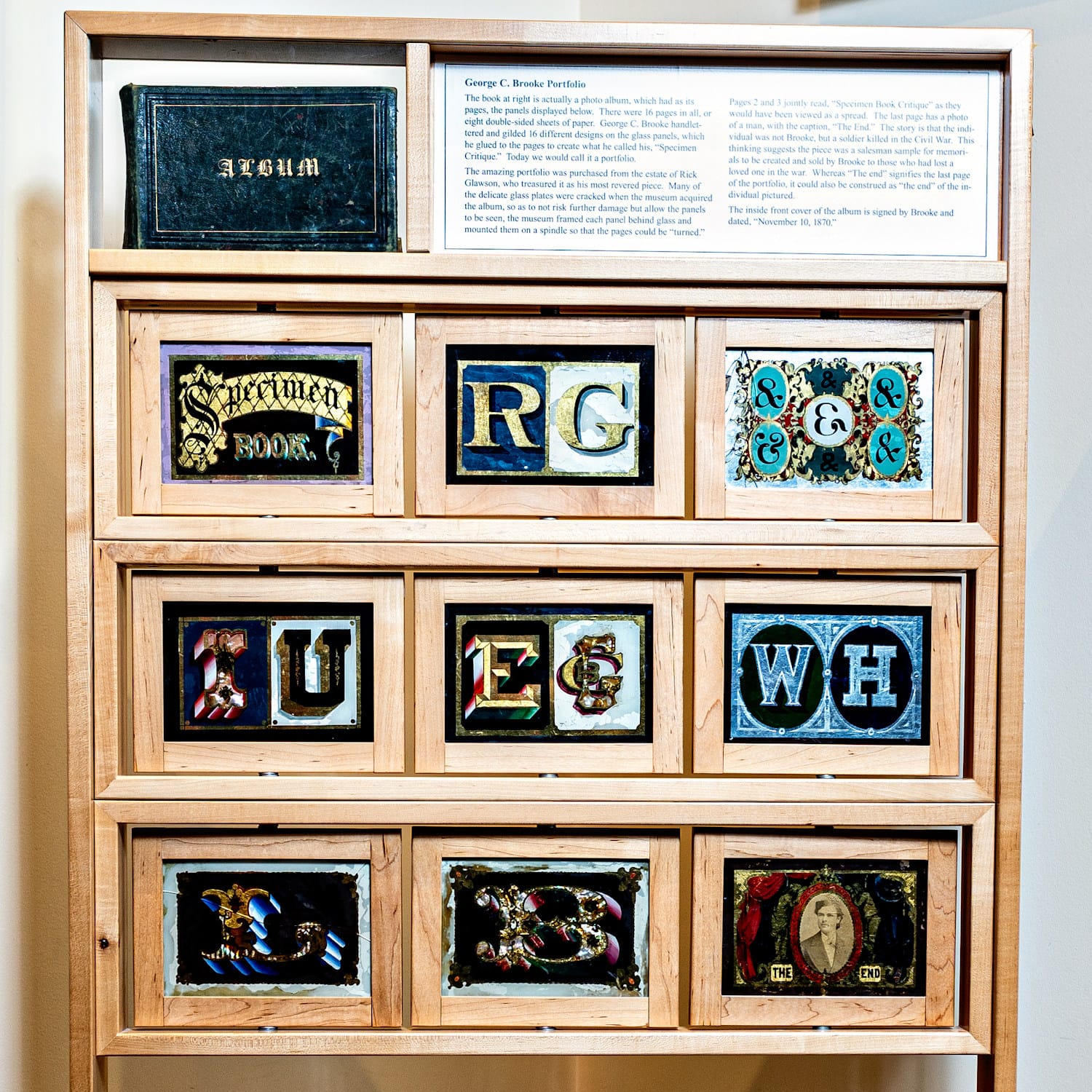 Wooden display case with a 3 x 3 array of small gilded glass panels below a narrative text panel.