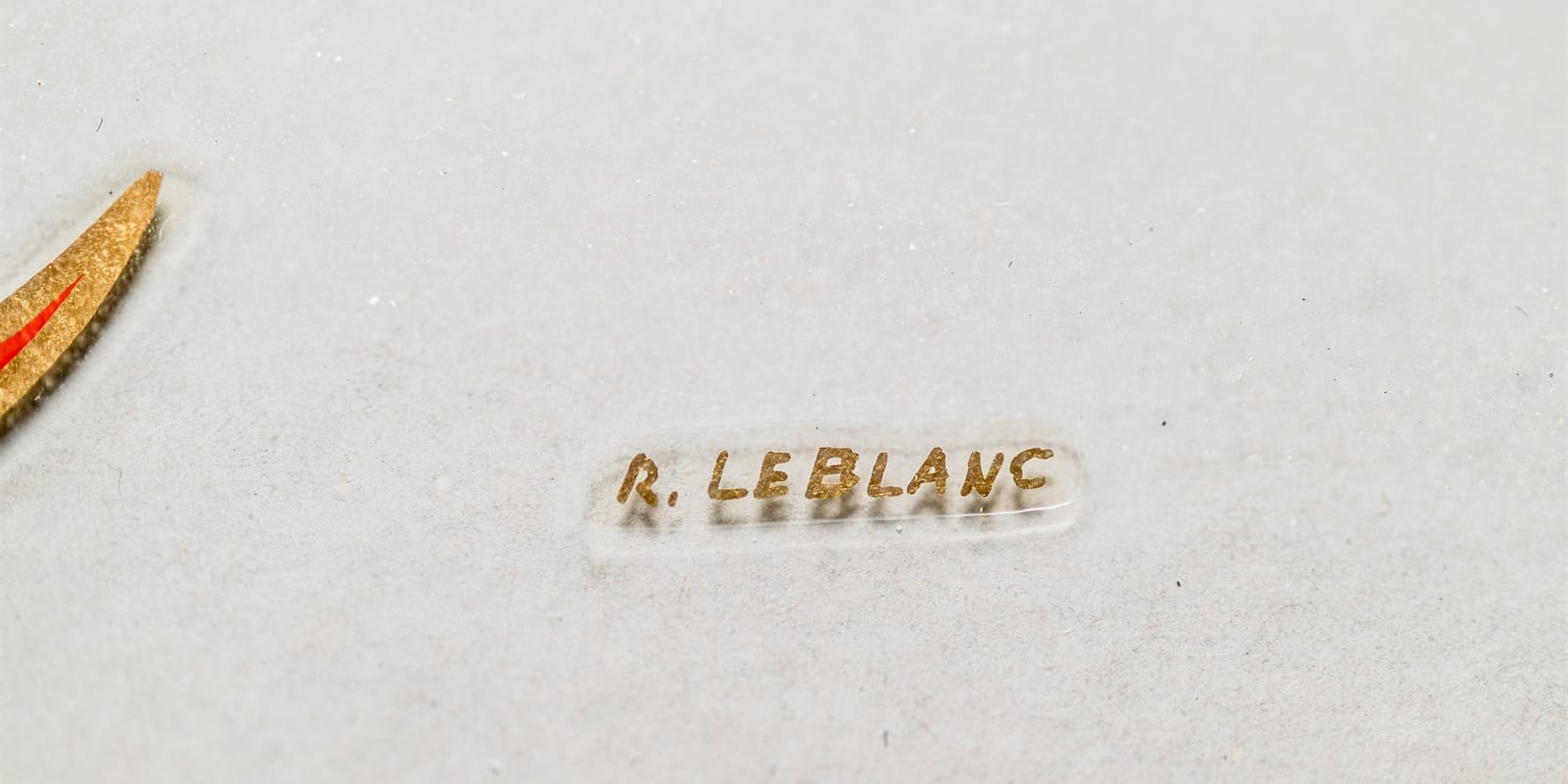 Miniscule single-stroke letters in gold reading "R. LEBLANC".