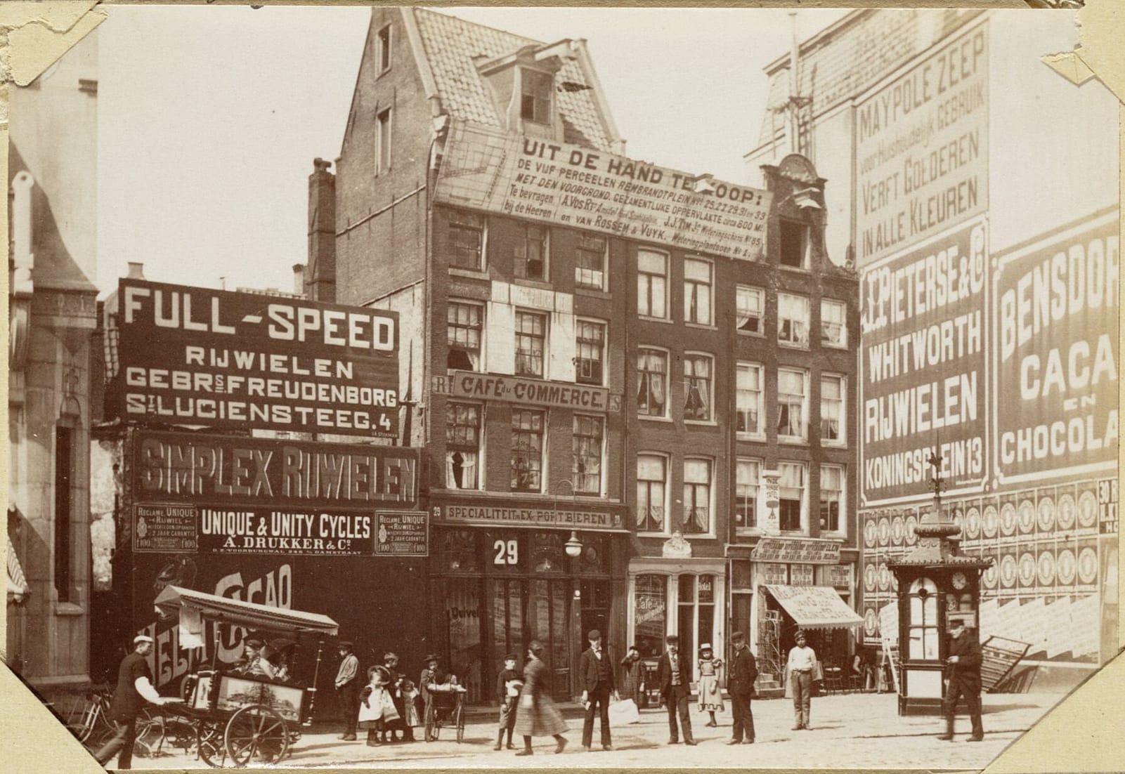 Archival photo of an urban setting with tall Dutch buildings covered in a variety of sign types including murals and mounted boards. The apparently unregulated proliferation of these lends a chaotic atmosphere to the scene. 