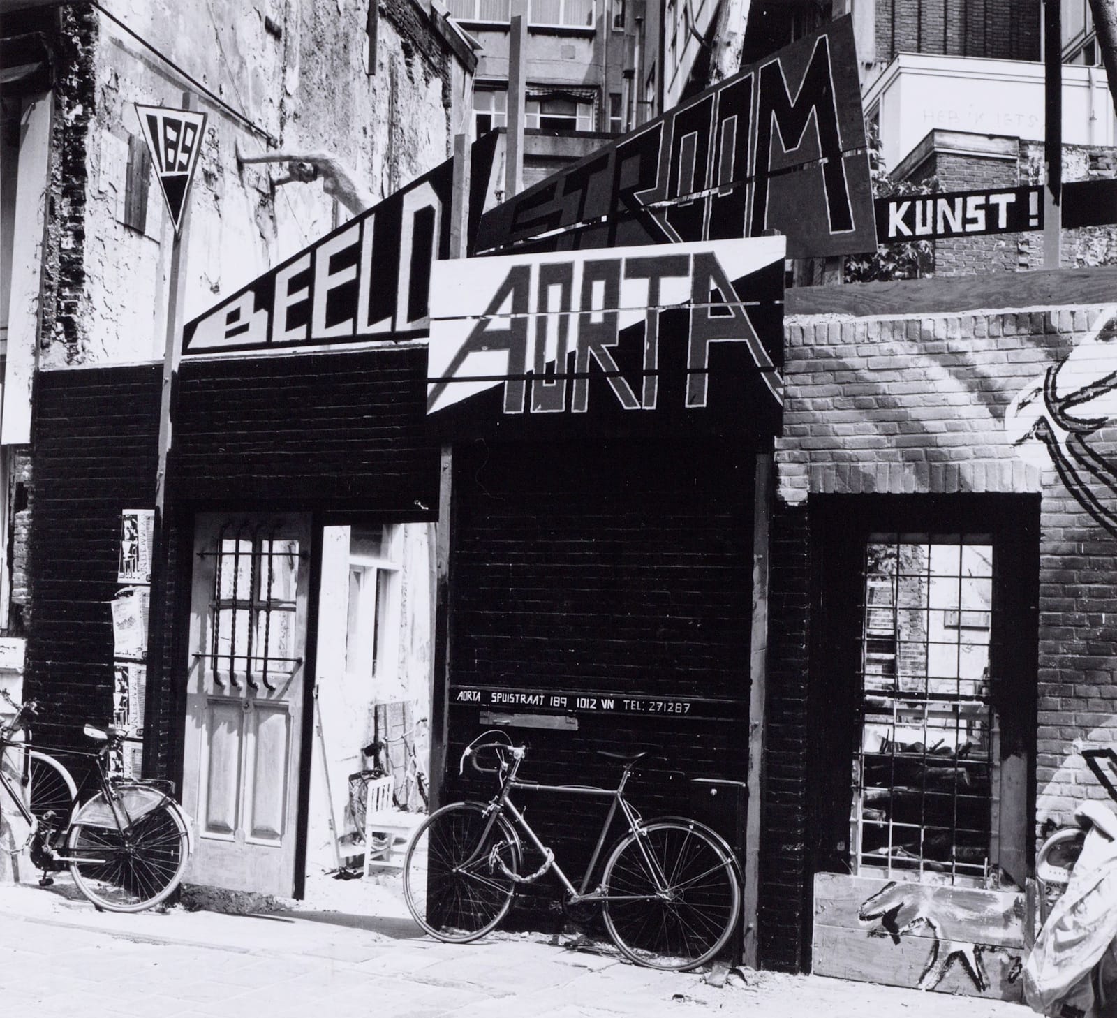 Low-rise building with home-made signs above that say "Beeld", "Stroom", "Aorta", and "Kunst" respectively.