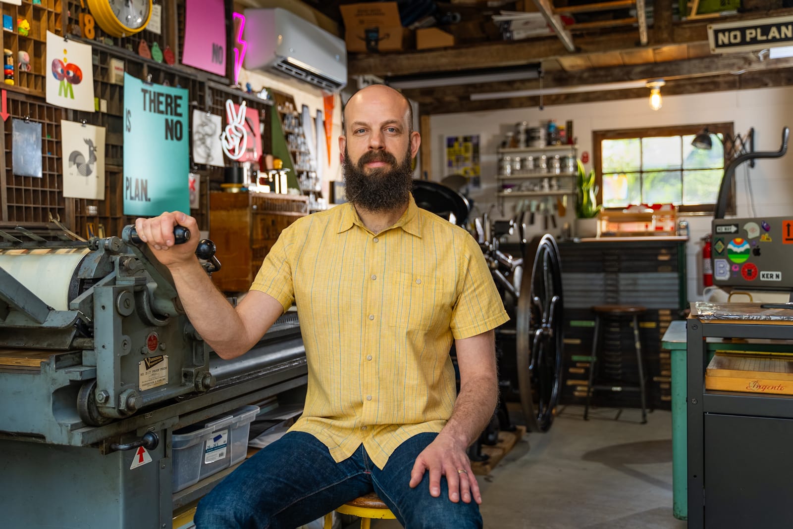 Portrait of a bearded man surrounded by printing equipment in a print-studio setting.