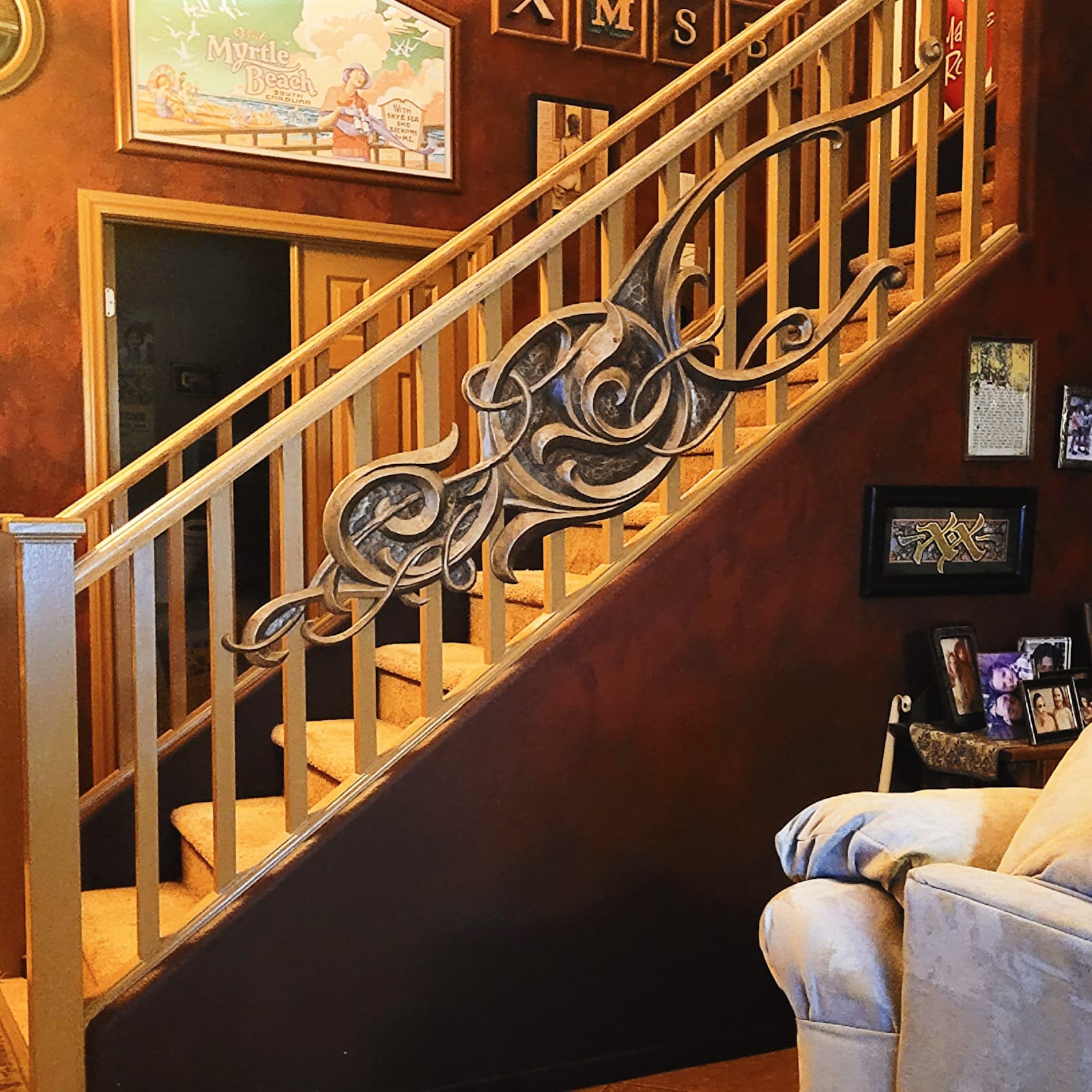 Homely scene showing a staircase with various framed sign-related artworks adorning the walls. Fixed to the bannister is the original piece of scrollwork running diagonally up the staircase.