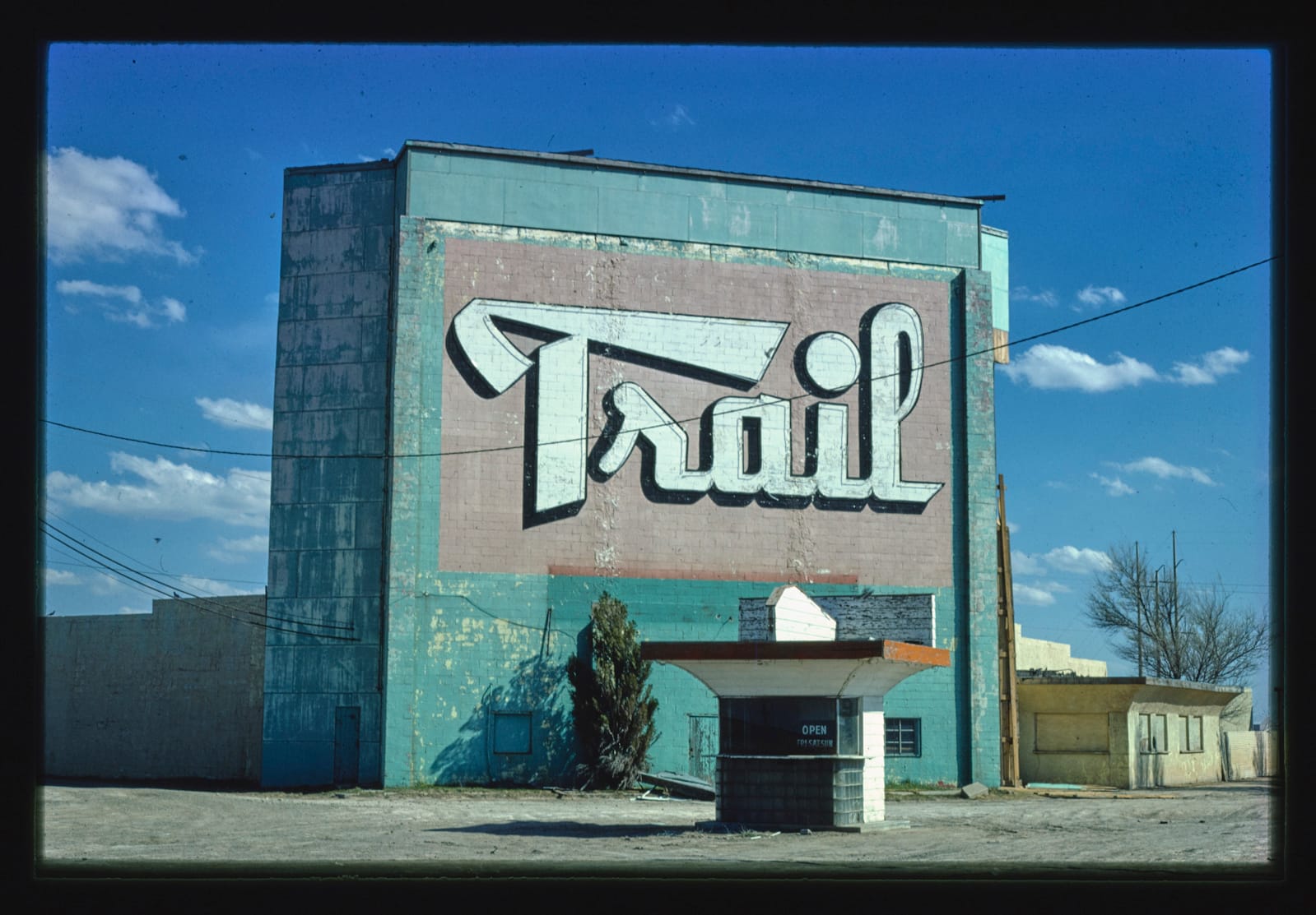 Large building with fading and damaged paintwork. A huge hand-painted sign simply reads "Trail" while a ticket kiosk occupies the ground in front.