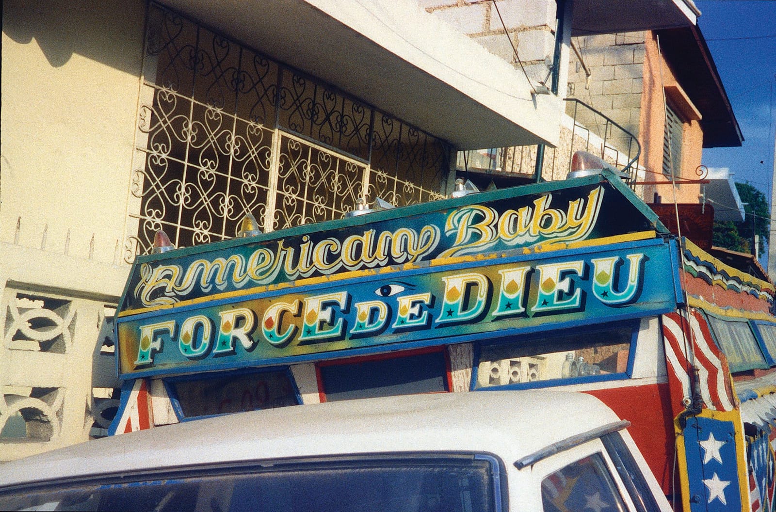 View of the board above the cabin of a transportation truck. The two panels contain the lettering for "American Baby, Force de Dieu".