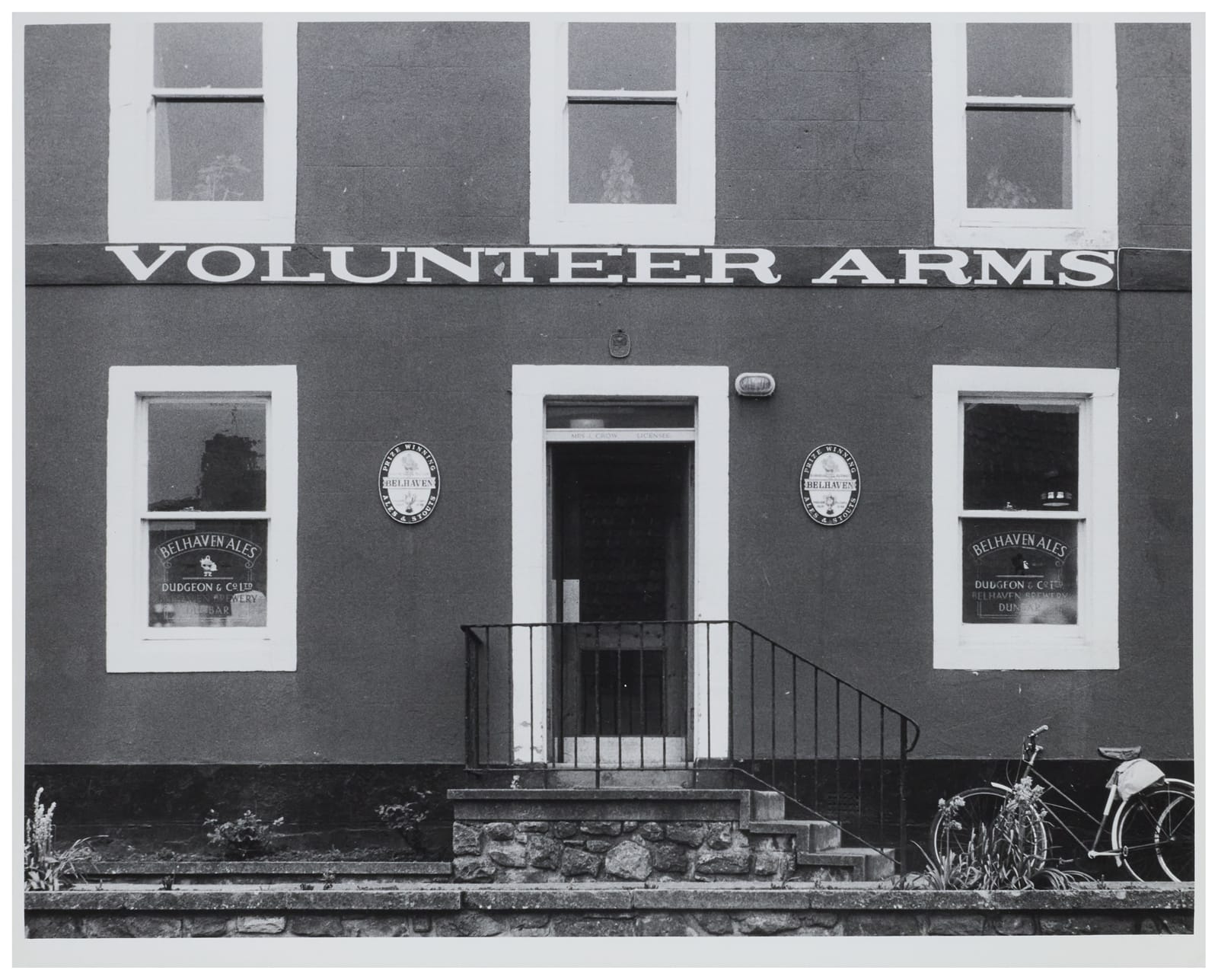 Photo of the front of a pub showing ground and first floors. A narrow strip below the first floor windows has simple serifed white lettering that says "Volunteer Arms".