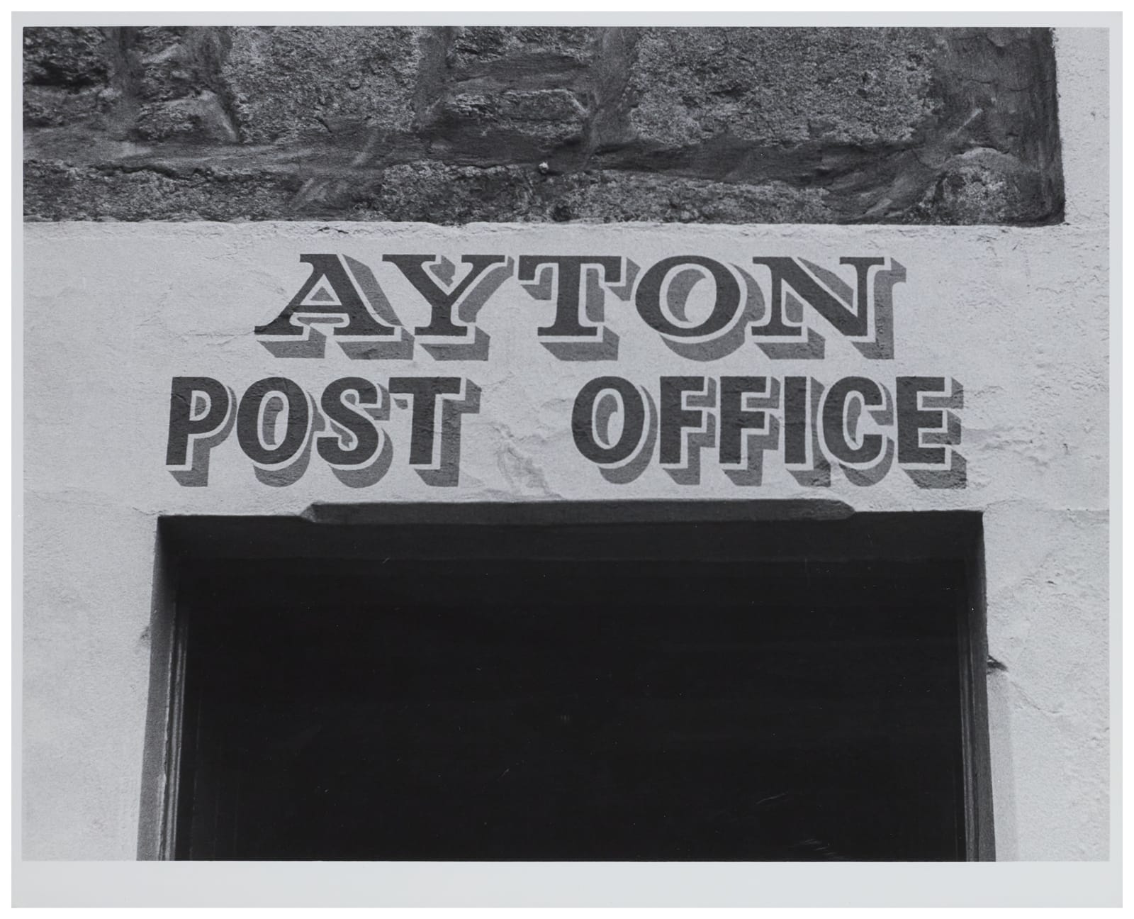 Two lines of hand-painted lettering in black with simple grey shade. "Ayton" has large serifs while "Post Office" on the line below is in a simple block. 