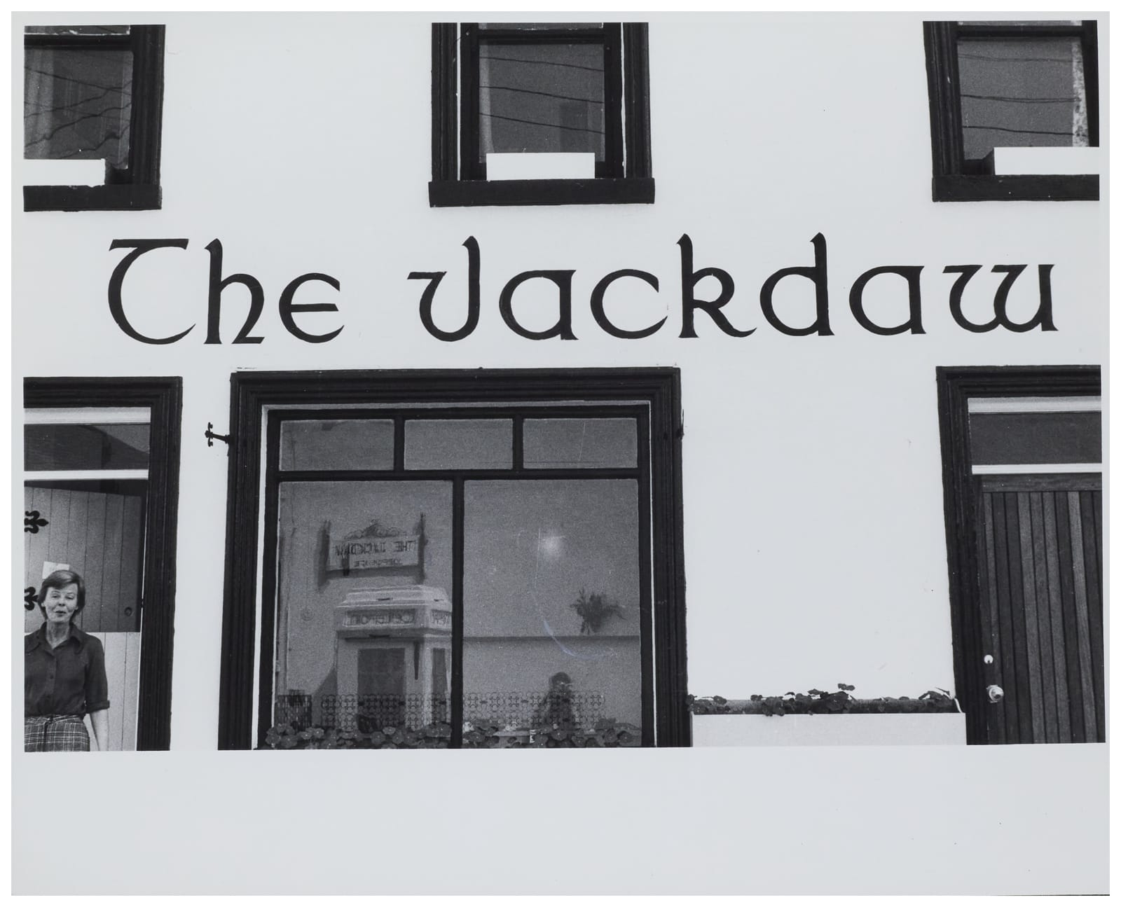 Bold black lettering for "The Jackdaw" on a whitewashed wall. A woman standing in the doorway is just visible in the lower left of the photo.