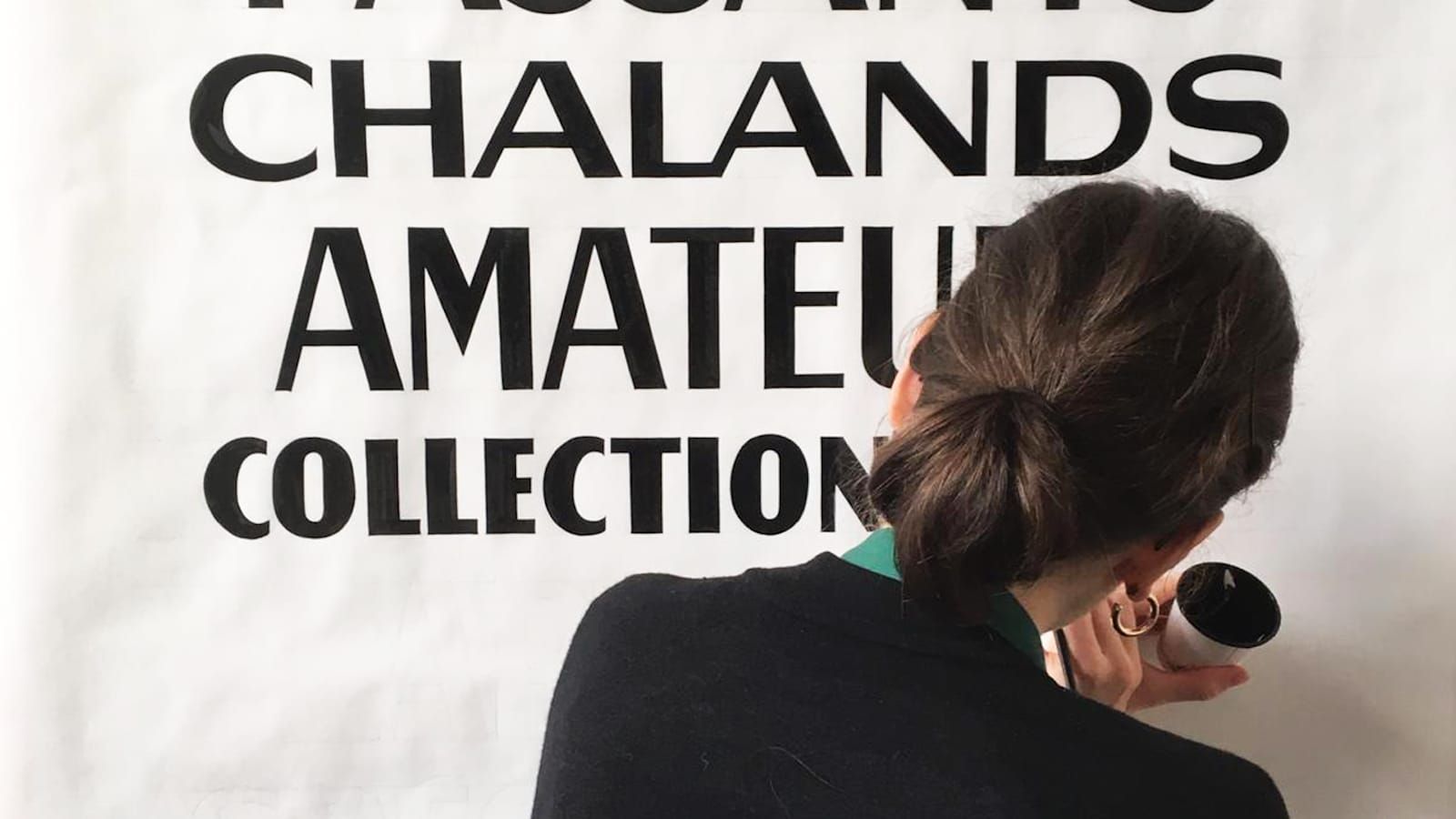 View from behind a woman's head as she paints black thick and thin lettering onto a white background.
