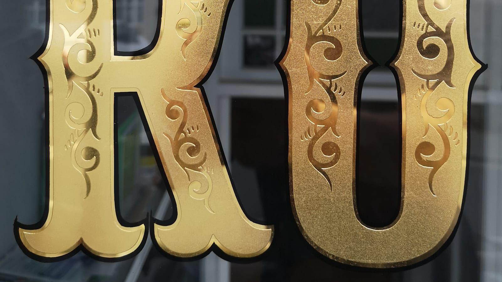 Lower two-thirds of bifurcated letters 'RO' with scrolls in their centres and gilded and outlined in black.