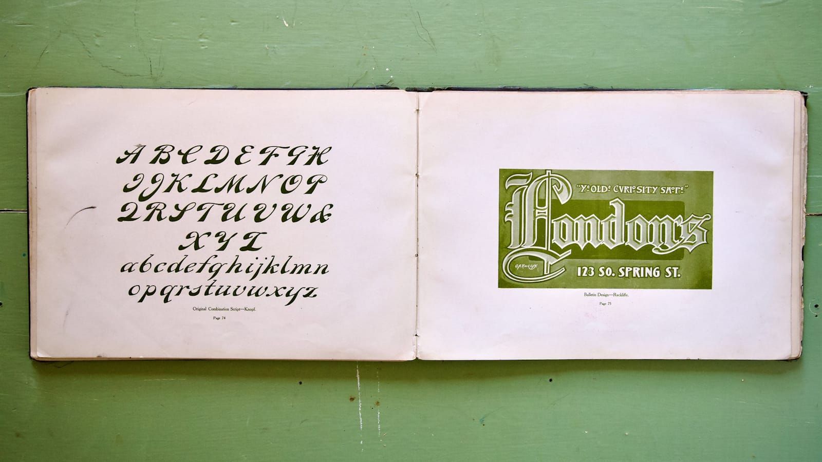 Old book spread out to show a script alphabet on the left and a sign design for London's Ye Olde Curiosity Shope on the right.