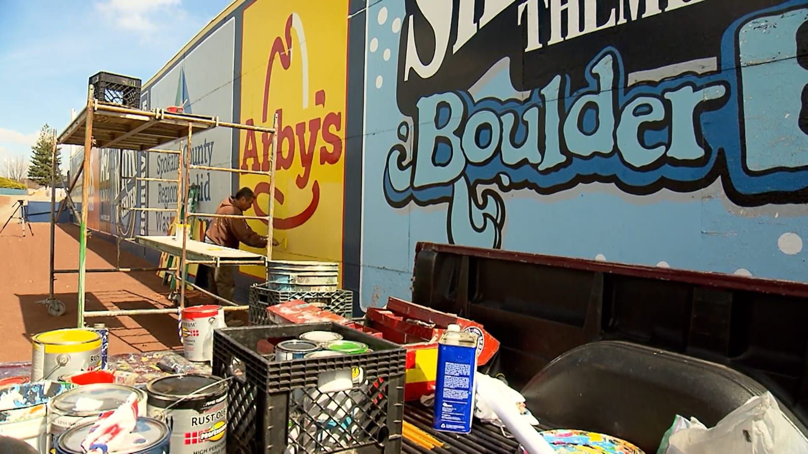 Man painting an Arby's sign on a ballpark fence adorned with other painted advertisements.