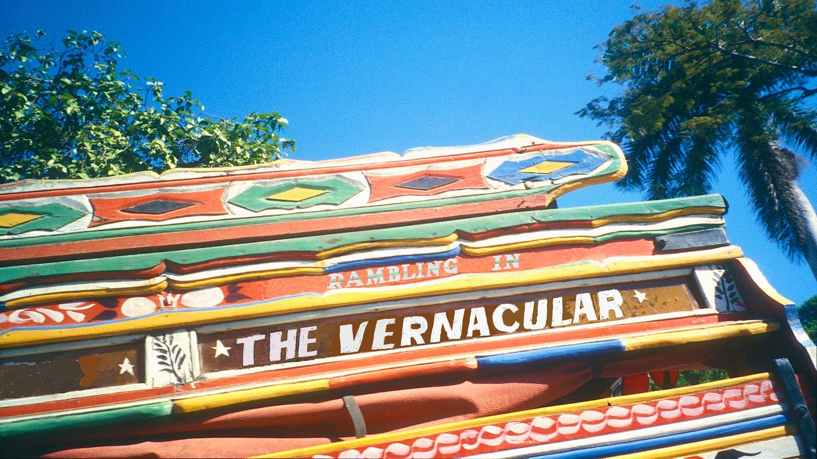 Portion of the side of a wooden vehicle with brightly coloured paint decorations. Lettering has been overlaid onto this reading "Rambling in the Vernacular".