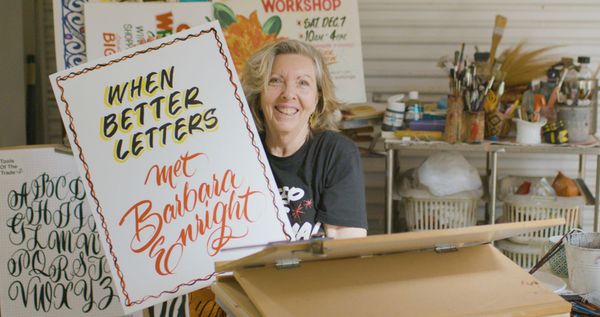 Woman in a studio holding a hand-painted showcard.