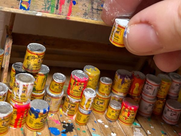 Close-up of a hand picking up a tiny tin of paint made to scale for a larger diorama.