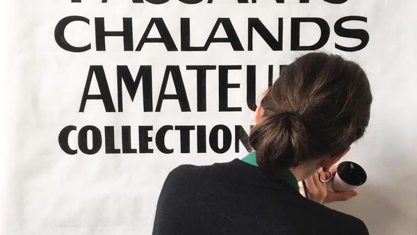 View from behind a woman's head as she paints black thick and thin lettering onto a white background.
