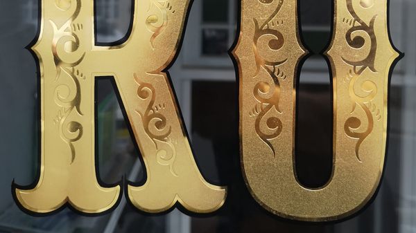 Lower two-thirds of bifurcated letters 'RO' with scrolls in their centres and gilded and outlined in black.