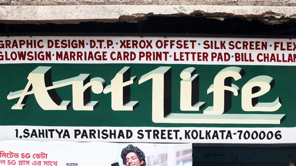 A painted sign for a DTP shop called “ArtLife”. The name is painted in white on a green background, and a list of their services is painted in red on white.