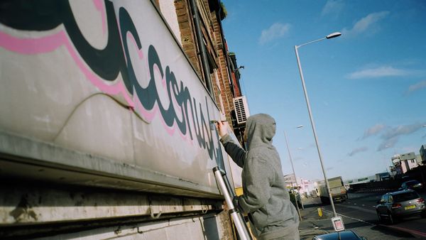 Hooded sign painter on a ladder working on a fascia sign on a busy road.