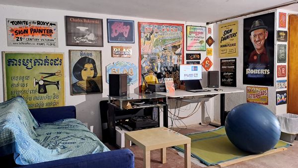 Desk in a corner of a room with the white walls filled with a variety of hand-painted signs of all sizes and types.