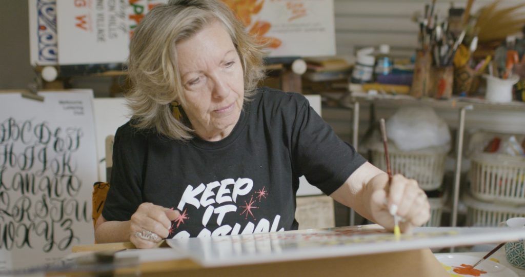 Woman at an easel in a studio painting lettering by hand.