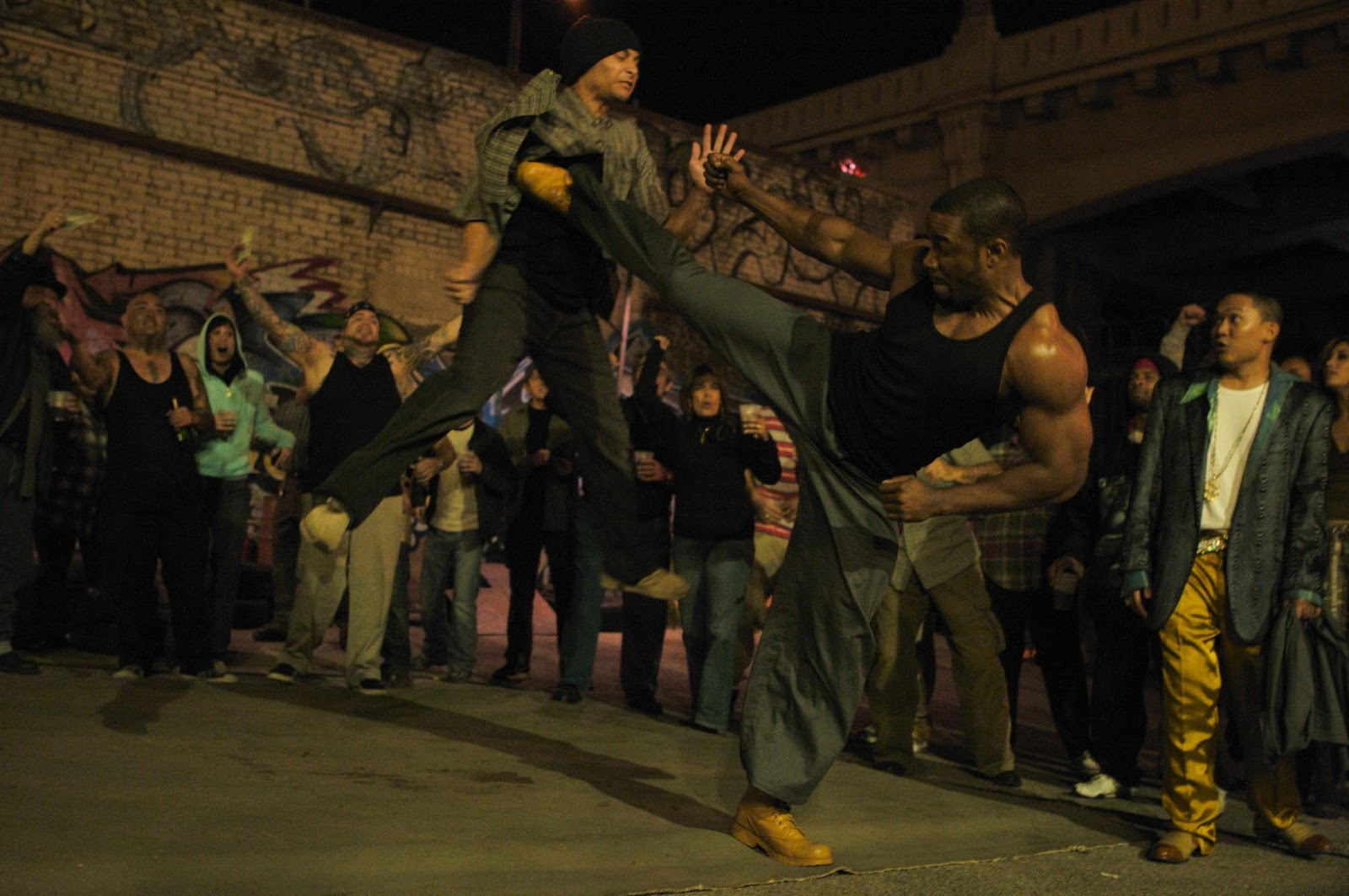 Michael Jai White kicks a man in mid-air in Blood and Bone as a crowd cheers on