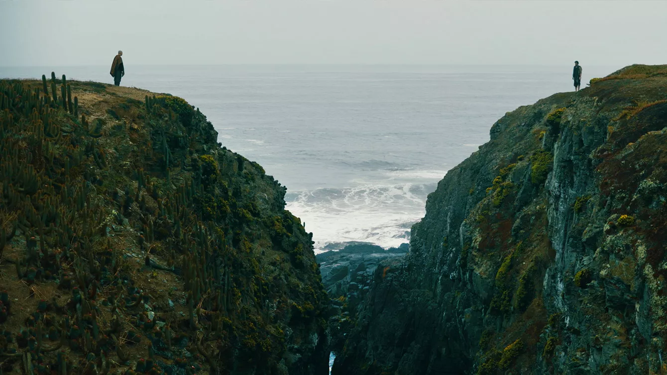 Two men stand on opposing cliffs with water between them in The Fist of the Condor