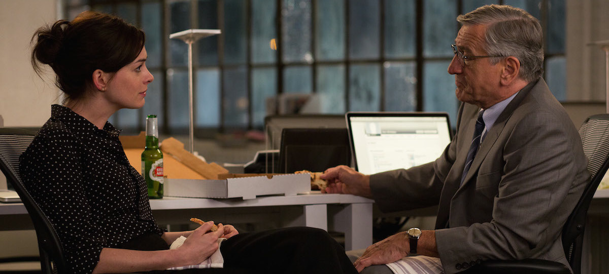 Anne Hathaway and Robert De Niro locked in a conversation while sitting at a desk in The Intern