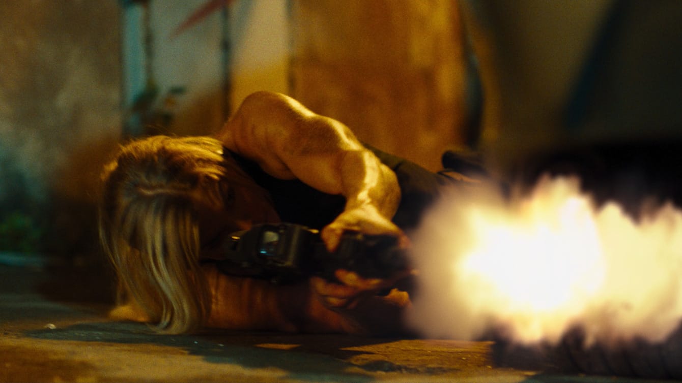 Brooke Ence fires an automatic rifle while leaning on her side on the ground in Affinity