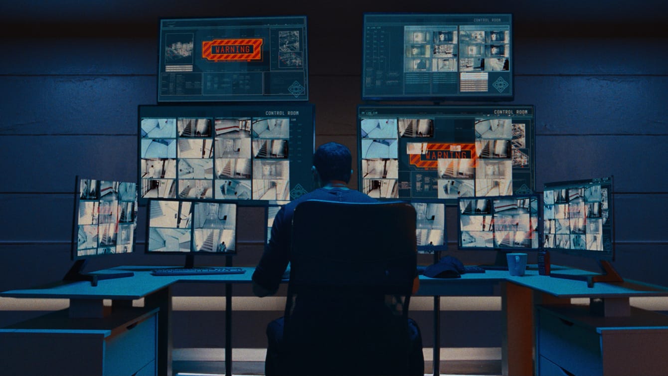 Marko Zaror sits at a desk with a lot of computer screens and security cam feeds in Affinity